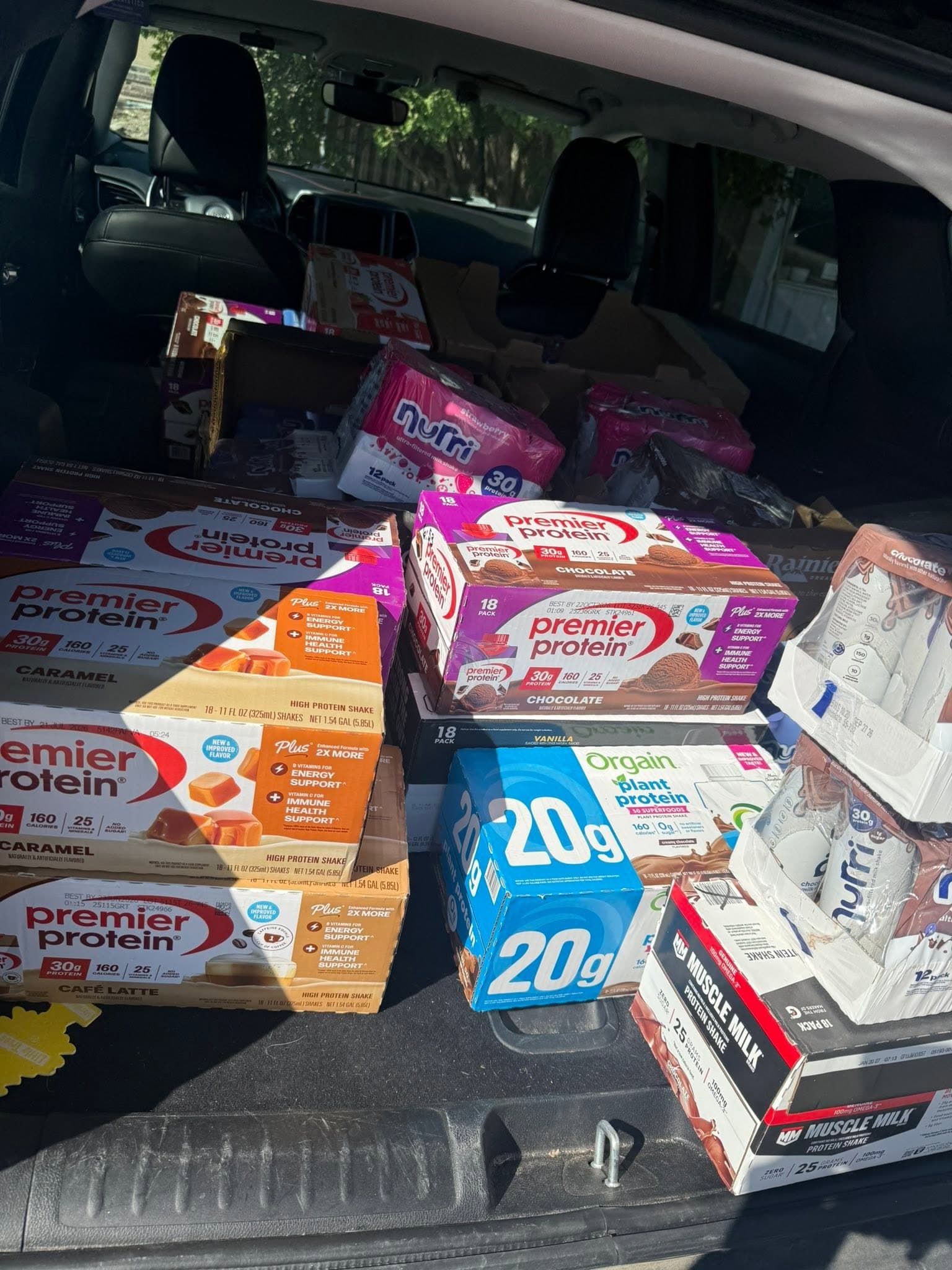 An open car trunk packed with cases of protein drinks, nutrition bars and milk.