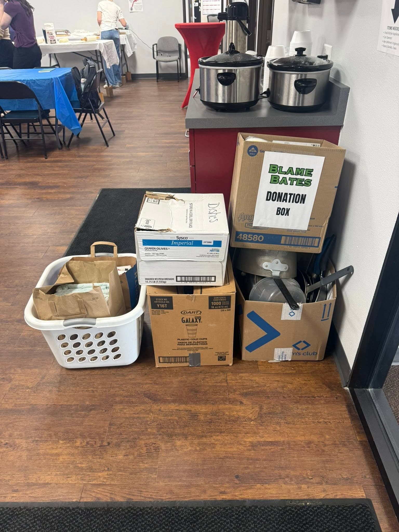 A carton labeled Blame Bates Donation Box beside baskets and boxes of donated goods in the office.