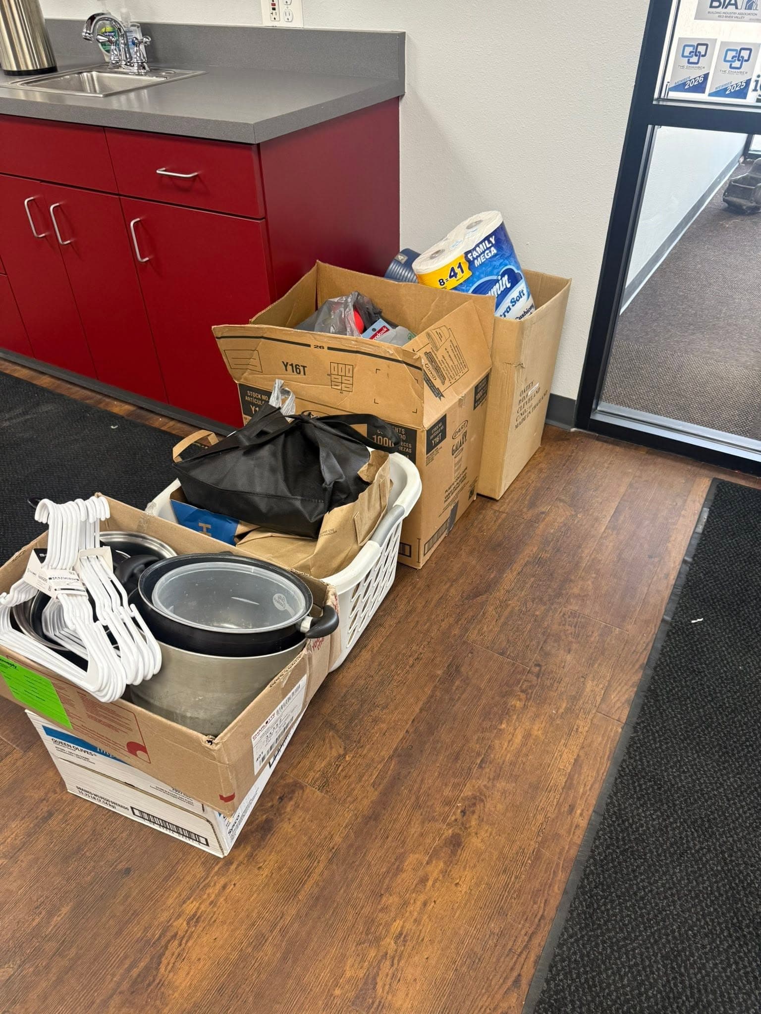 Boxes of hygiene supplies, cookware and clothes hangers on the office floor.