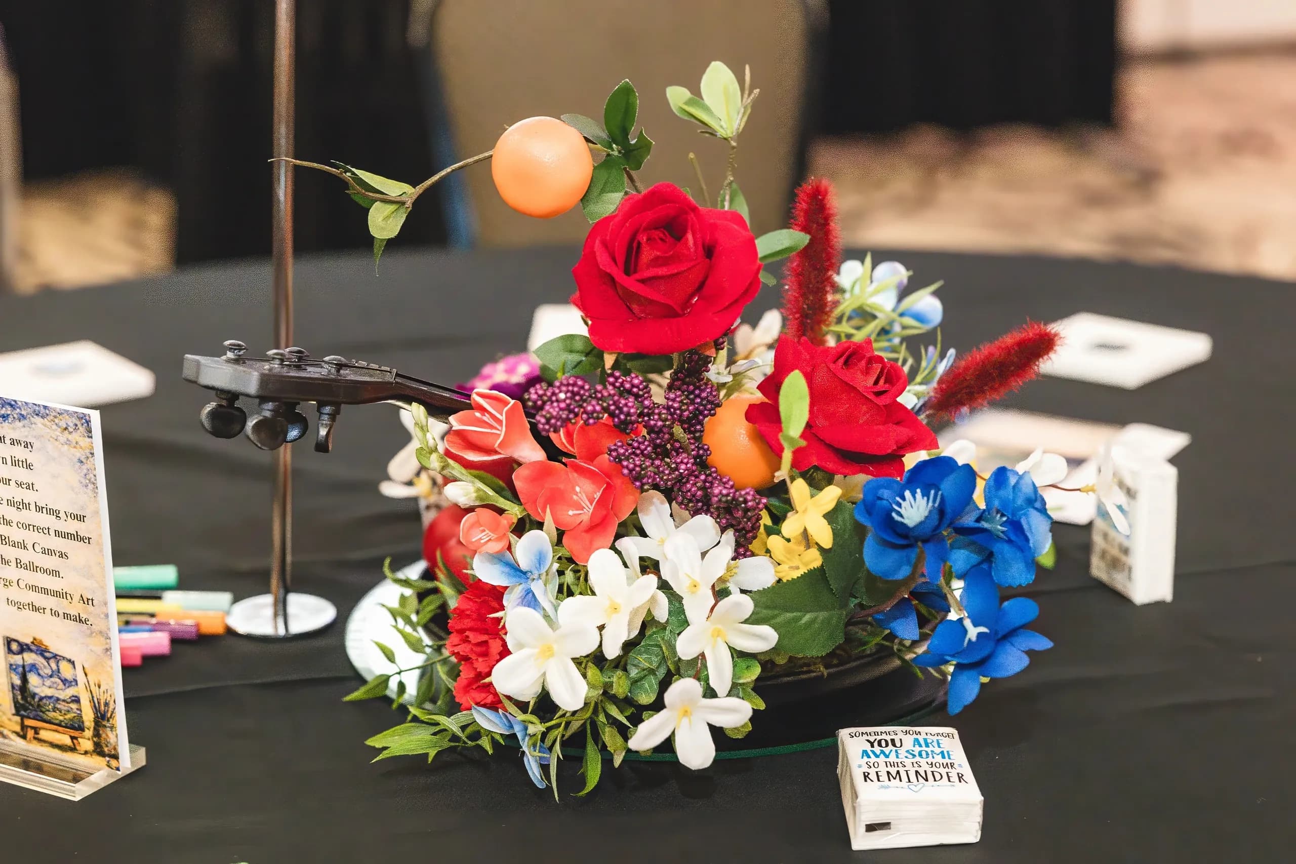 A bright floral centerpiece surrounded by art supplies on a banquet table.